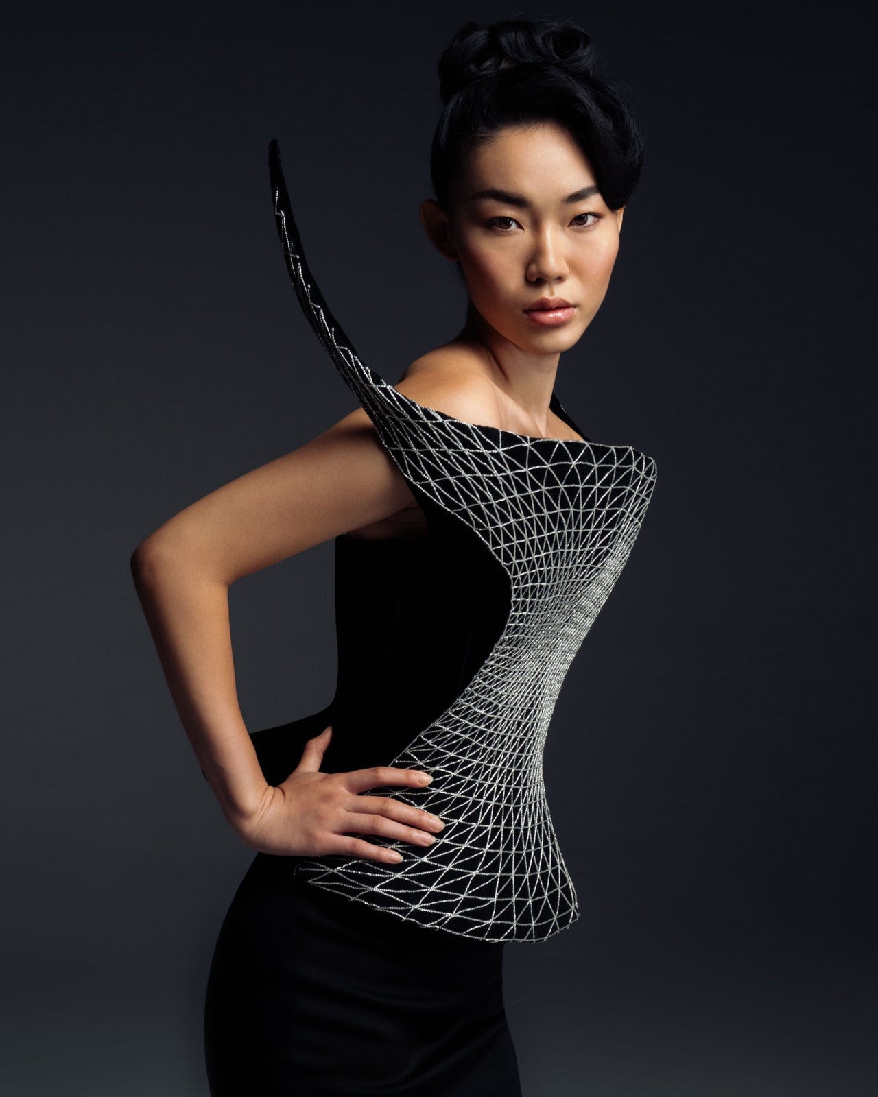 Model wearing a futuristic black and gray top against a dark background