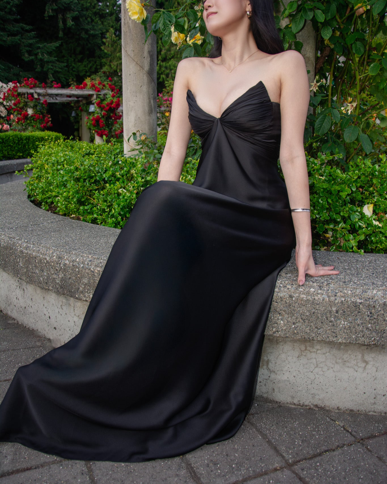 Woman in a black evening gown sitting on steps with greenery and flowers in the background