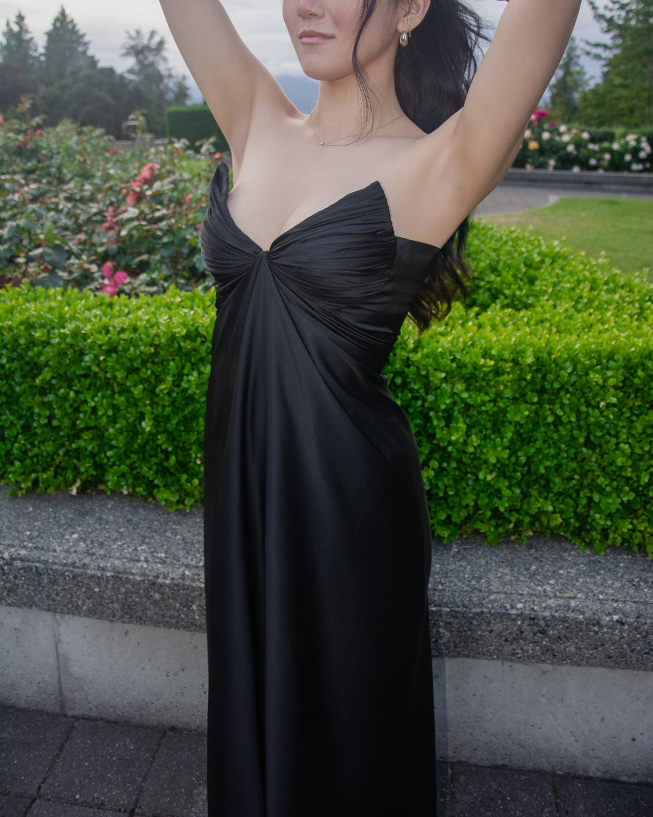 Woman wearing a black strapless dress standing outdoors with greenery in the background