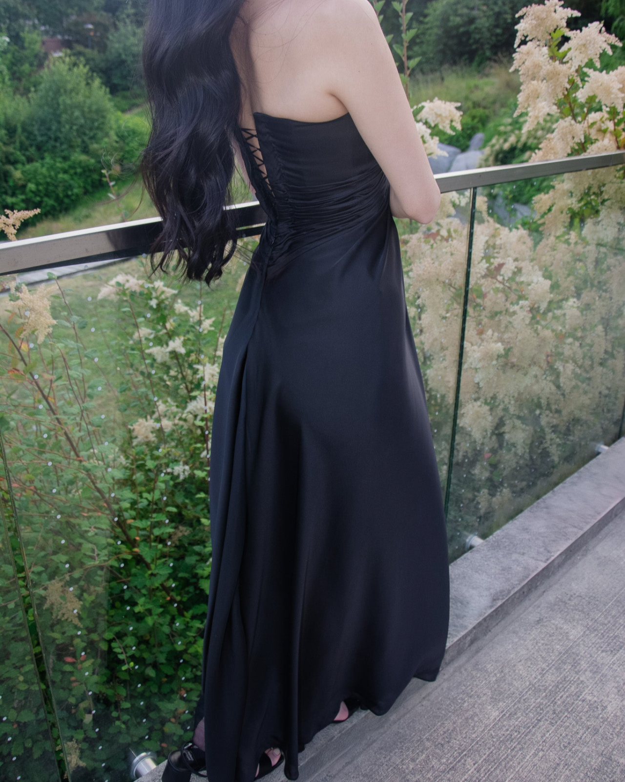 Woman in a black strapless dress standing on a balcony with greenery in the background