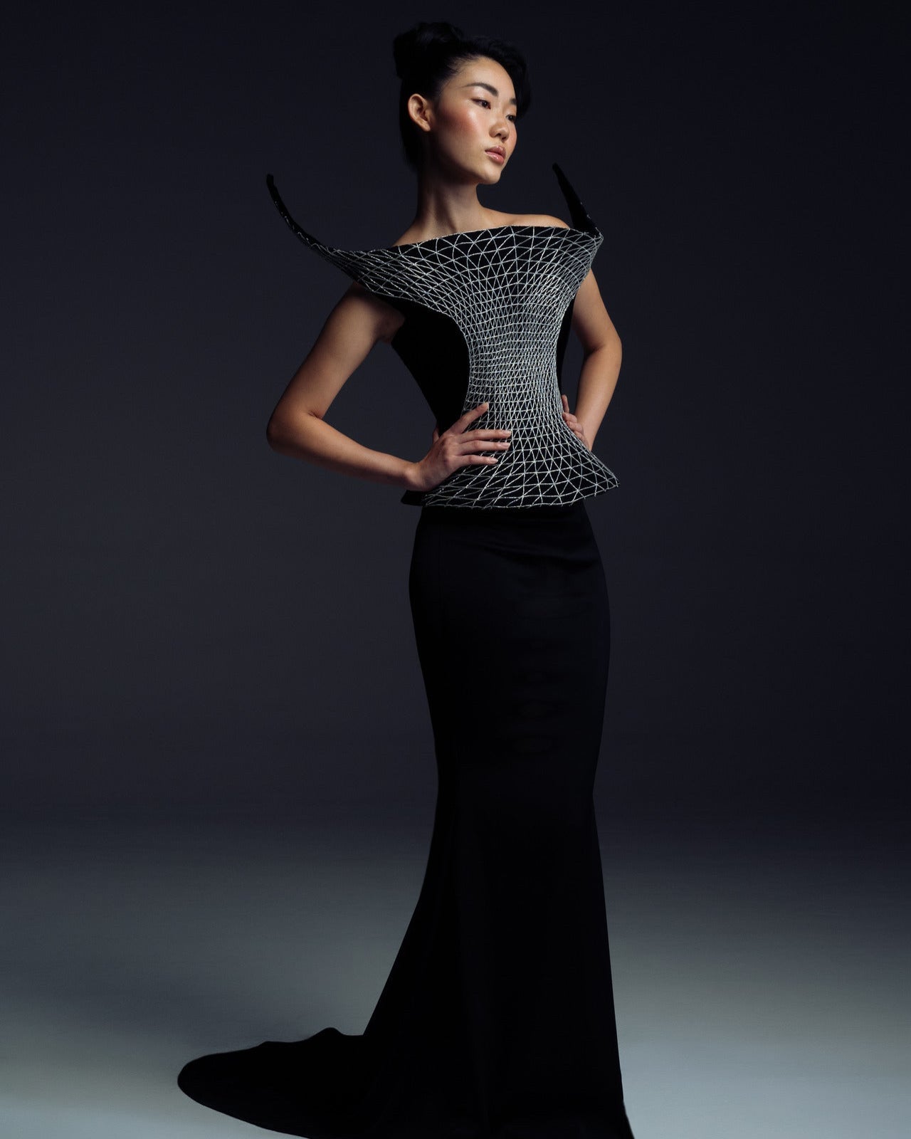 Woman wearing a futuristic black dress with geometric patterns against a dark background