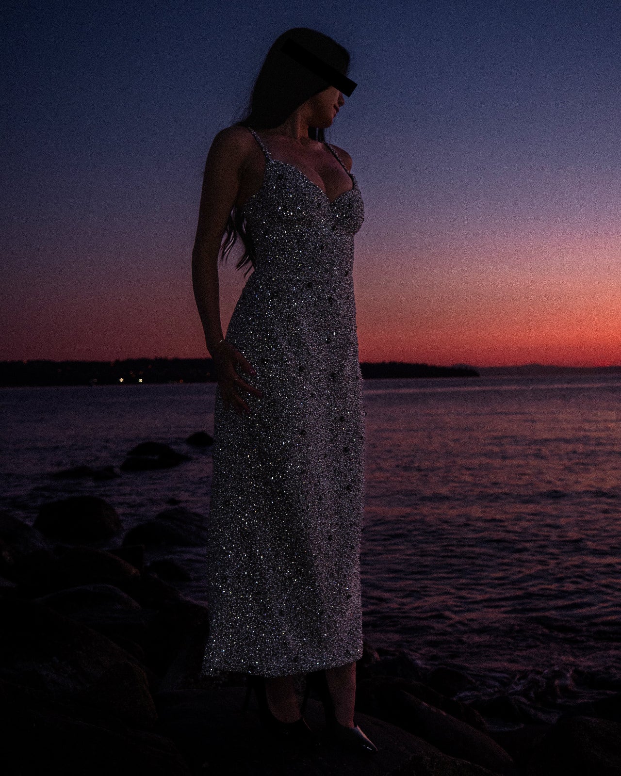 Woman in a sparkly dress standing on a beach at sunset.